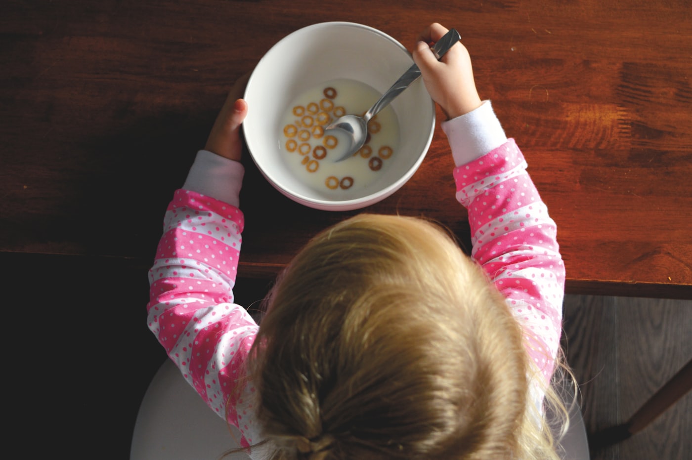 Criança a comer cereais de uma taça branca à mesa